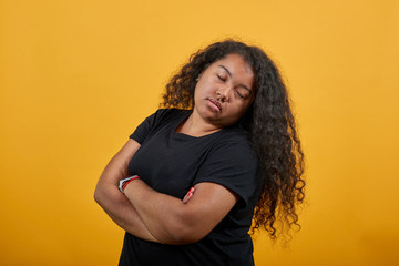 Obraz premium Serious young woman with overweight keeping hands crossed, closed eyes, having nice clock over isolated orange background wearing fashion black shirt. People lifestyle concepte.