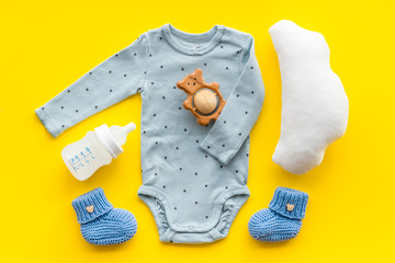 Cute baby clothes - suit - booties and accessories on yellow table top-down