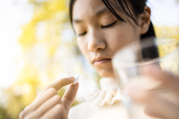 Sick asian child girl holding pill and glass of fresh water in hand,sad female teen taking medicine...