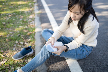 Obraz premium Asian child girl sitting on the floor and takes off a sneakers,hold her sore spot,sad female teenage rubbing and massaging her painful foot,fatigue,achy and tired from walk,run or stand for a long day