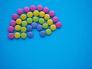 Rainbow shape made of colorful candy sweets on blue solid background with copy space.