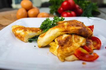 Traditional omelet with vegetables, spinach, tomatoes and herbs on a wooden table in a restaurant.