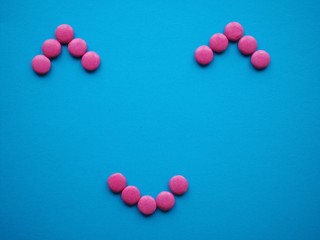 Happy smiley shape made of pink candy sweets on blue solid background with copy space.