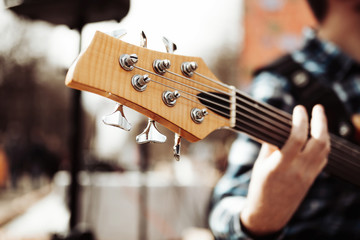 Photo of musician playng on six string fretless bass guitar on the street in front of people.