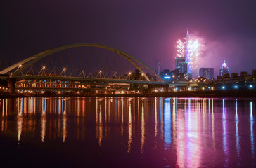 Fototapeta na wymiar New Year fireworks light up the Taipei City skyline, casting reflections in the Keelung River