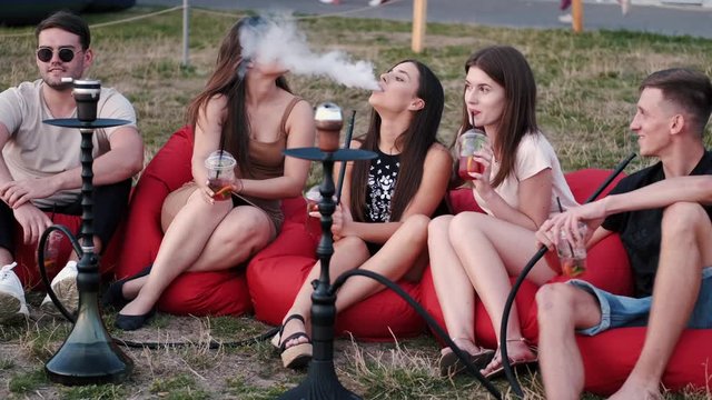 European friends are chilling out and smoking shisha at the beach. They are sittin in the beanbags and drinking cocktails.