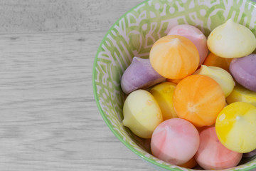 Meringues, various colours, in a green patterned bowl dish.  Grey wood background