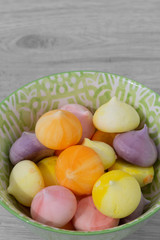 Meringues, various colours, in a green patterned bowl dish.  Grey wood background