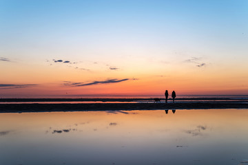 two girls look at a beautiful sunset while on the shallows at low tide