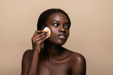 Close up portrait of an attractive african american woman removing makeup with sponge isolated on...