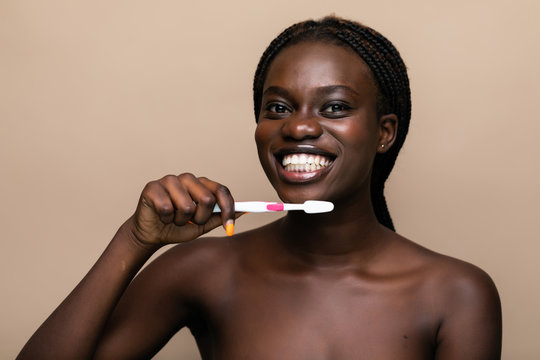 Close Up Of A Young African American Woman Brushing Her Teeth With A Toothbrush Isolated On Beige