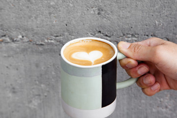Hot coffee art latte in hand and concrete wall
