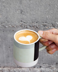 Hot coffee art latte in hand and concrete wall