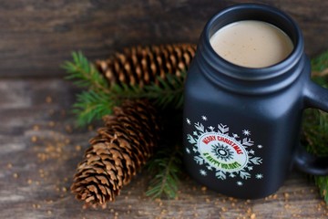 Christmas, new year concept with mug of hot coffee with milk against rustic wooden background with spruce branches and cones. Selective focus.
