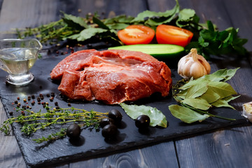 On a dark countertop, a large piece of raw beef, garnished with bay leaves, pepper