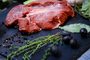 On a dark countertop, a large piece of raw beef, garnished with bay leaves, pepper