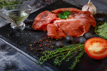 On a dark countertop, a large piece of raw beef, garnished with bay leaves, pepper