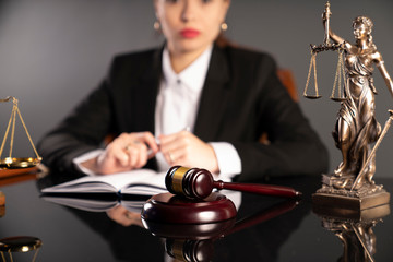 Young lawyer during work in chamber. Gavel, scale and Themis statue on the table.