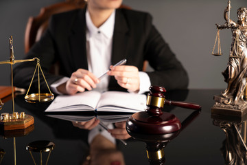 Young lawyer during work in chamber. Gavel, scale and Themis statue on the table.