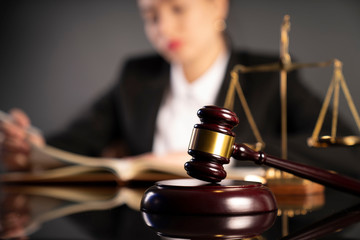 Young lawyer during work in chamber. Gavel, scale and Themis statue on the table.