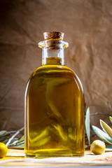 Extra virgin olive oil in glass bottle. It includes olive leaves and branches. Rustic Background. Front view.