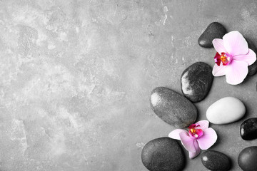 Fototapeta na wymiar Stones with orchid flowers and space for text on grey background, flat lay. Zen lifestyle