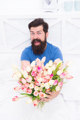 Fresh flowers. Bearded hipster in bed. Spring in bedroom. Man hold tulips bouquet while relaxing in bed. Flowers delivery service. Birthday anniversary holiday. Make surprise concept. Gift for spouse