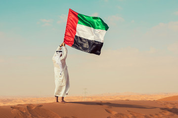 Proud arabian Emirati man holding a UAE flag in the desert