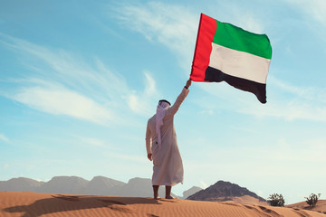 Proud arabian Emirati man holding a UAE flag in the desert