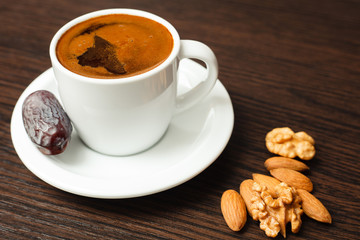 Close-up of single white cup of coffee and almonds on dark wooden table. High angle view