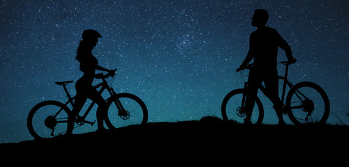 Obraz premium Two silhouettes of cyclists on a sunset background. Athletic guy and a girl on modern mountain bikes go to each other.