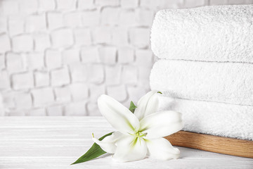 Fototapeta na wymiar Stack of clean bath towels and beautiful flower on white wooden table. Space for text