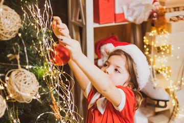 Christmas toy - girl is decorating the Christmas tree. Christmas kid decorating Christmas tree with...