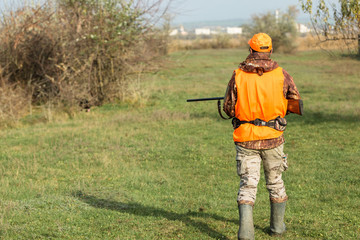 A man with a gun in his hands and an orange vest on a pheasant hunt in a wooded area in cloudy...