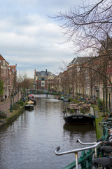 Canal in Leiden, the Netherlands, with a bridge over it and canal houses on either side, photographed from a bridge with a lot of bicycles.