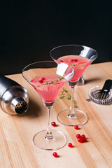 Two martini glasses filled with red color cranberry cocktail and barmen tools on the wooden table.