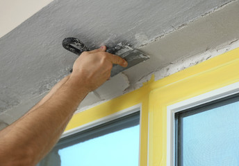 Man plastering window area with putty knife indoors, closeup. Interior repair