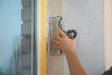 Man plastering window area with putty knife indoors, closeup. Interior repair