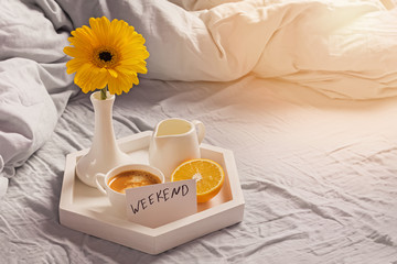 Tray with coffee, milk, orange, yellow flower in a vase and card with text Weekend