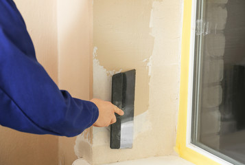 Professional worker plastering window area with putty knife indoors, closeup. Interior repair