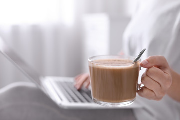 Woman with cup of morning coffee working on laptop indoors, closeup. Space for text