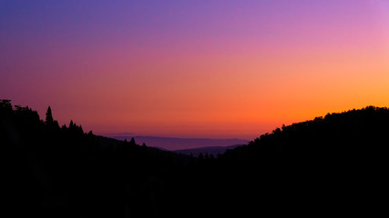 silhouette of trees and hills under orange and  purple sky during sunrise