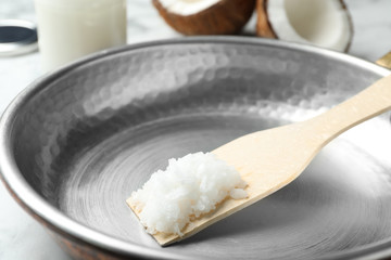 Fototapeta na wymiar Frying pan with coconut oil and wooden spatula on white marble table, closeup. Healthy cooking