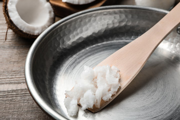 Frying pan with coconut oil and wooden spatula on wooden table, closeup. Healthy cooking