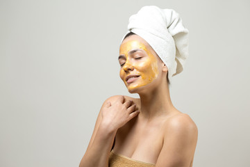 Beauty portrait of woman in white towel on head with gold nourishing mask on face. Skincare cleansing eco organic cosmetic spa relax concept.