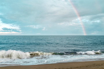 rainbow over the sea. light surf and sandy beach under the rainbow