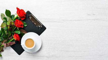 Cup of coffee and red roses on a white table. Top view. Free space for your text.