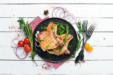Pork steak on a bone with rosemary and greens in a black plate. Top view. Free copy space.