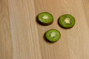 Three sliced kiwi slices on a light brown wooden surface