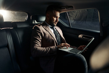 guy businessman in car with laptop and phone